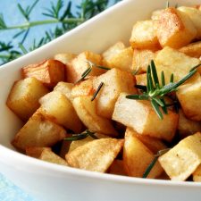 crispy roasted potatoes in a white bowl with rosemary