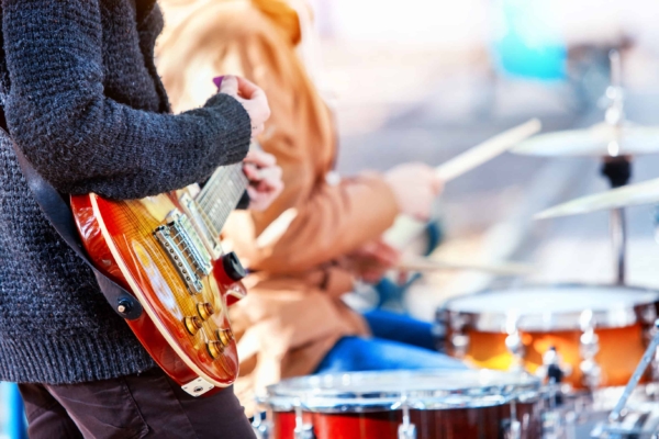 Man playing a guitar with a drummer in the background at a summer music festival