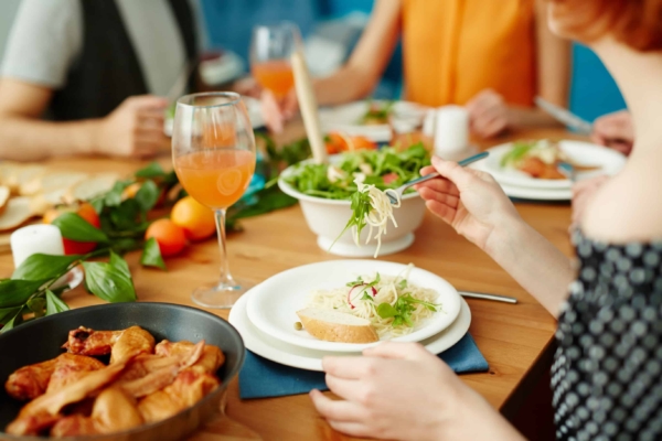 People eating around a table outdoors, salad on a white plate, blue napkin