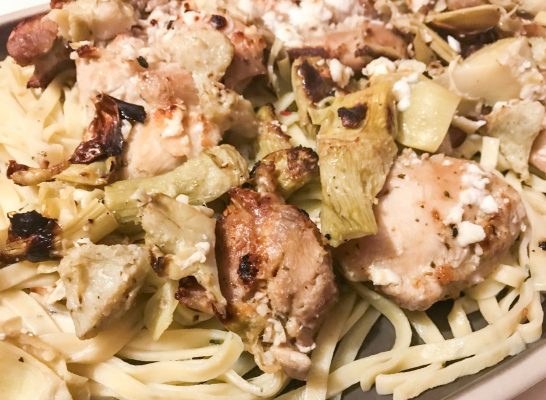 Gray serving platter containing fresh pasta, artichokes, broiled chicken thighs, and feta cheese