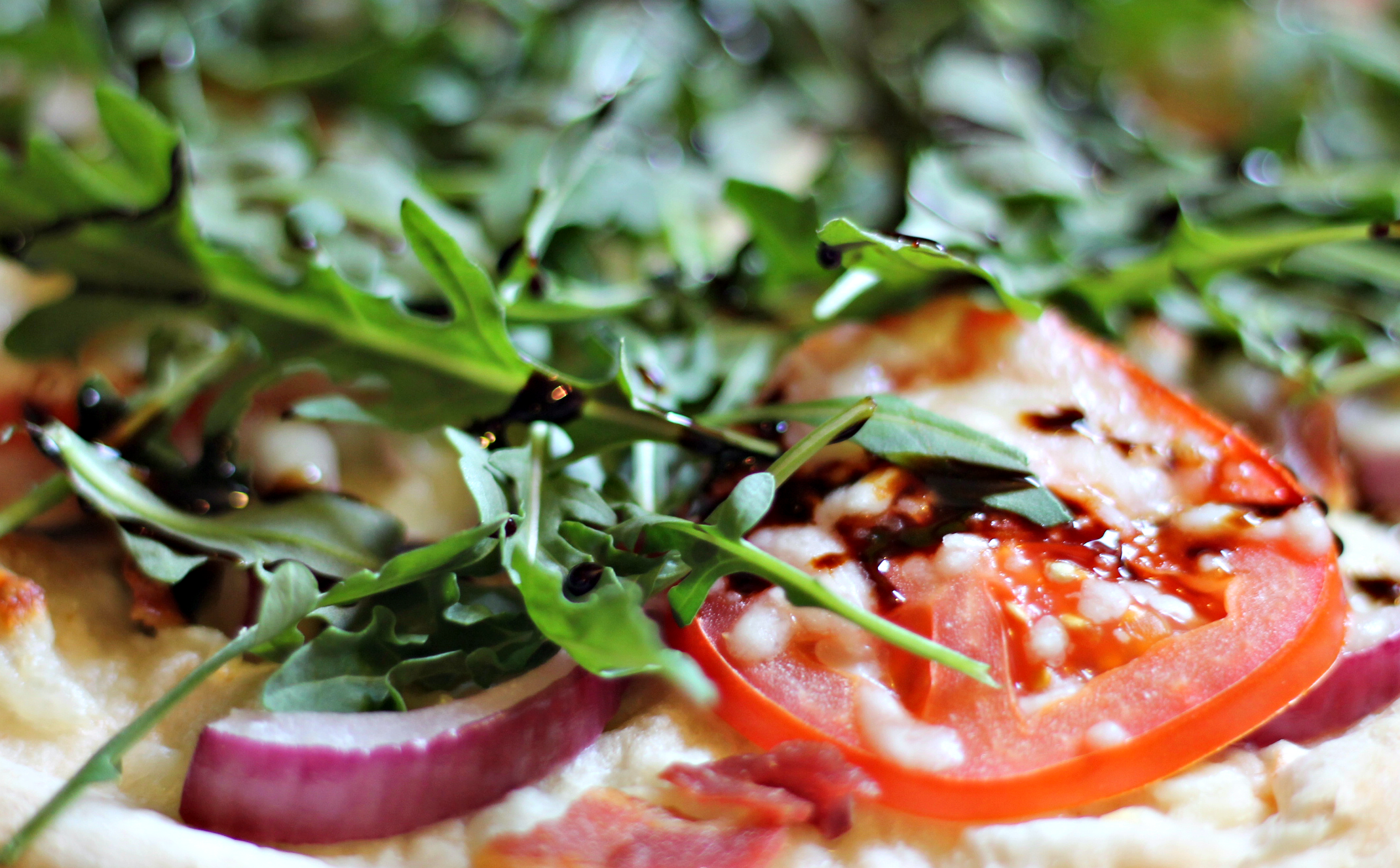 close-up of BLT Pizza with bacon, tomato, arugula, red onion, and balsamic glaze