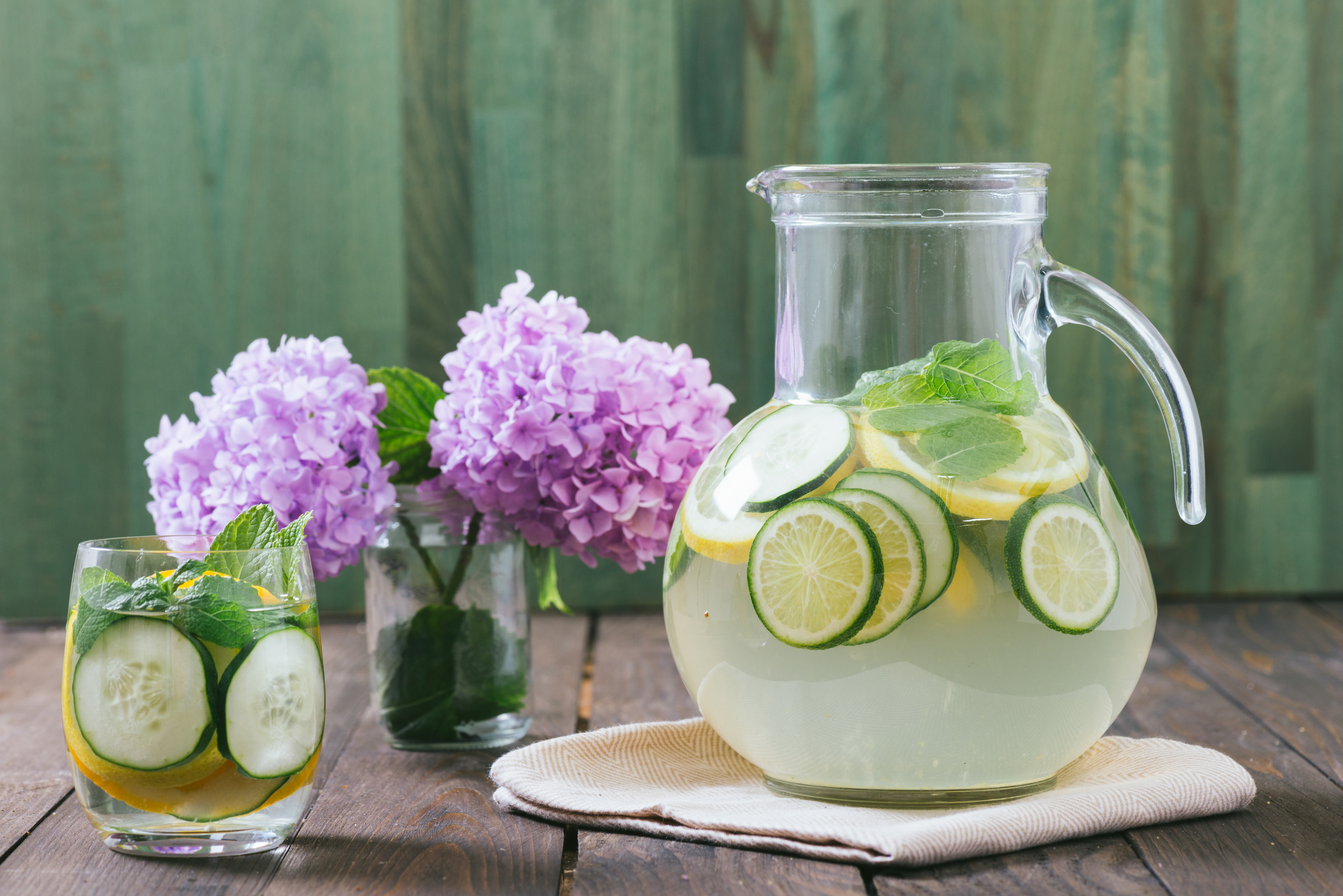 glass pitcher of water with lime slices on a table with purple hydrangias in a vase