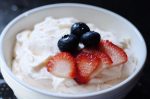 White bowl of fruit dip with strawberries and blueberries surrounded by apples, pineapple, blueberries, and strawberries