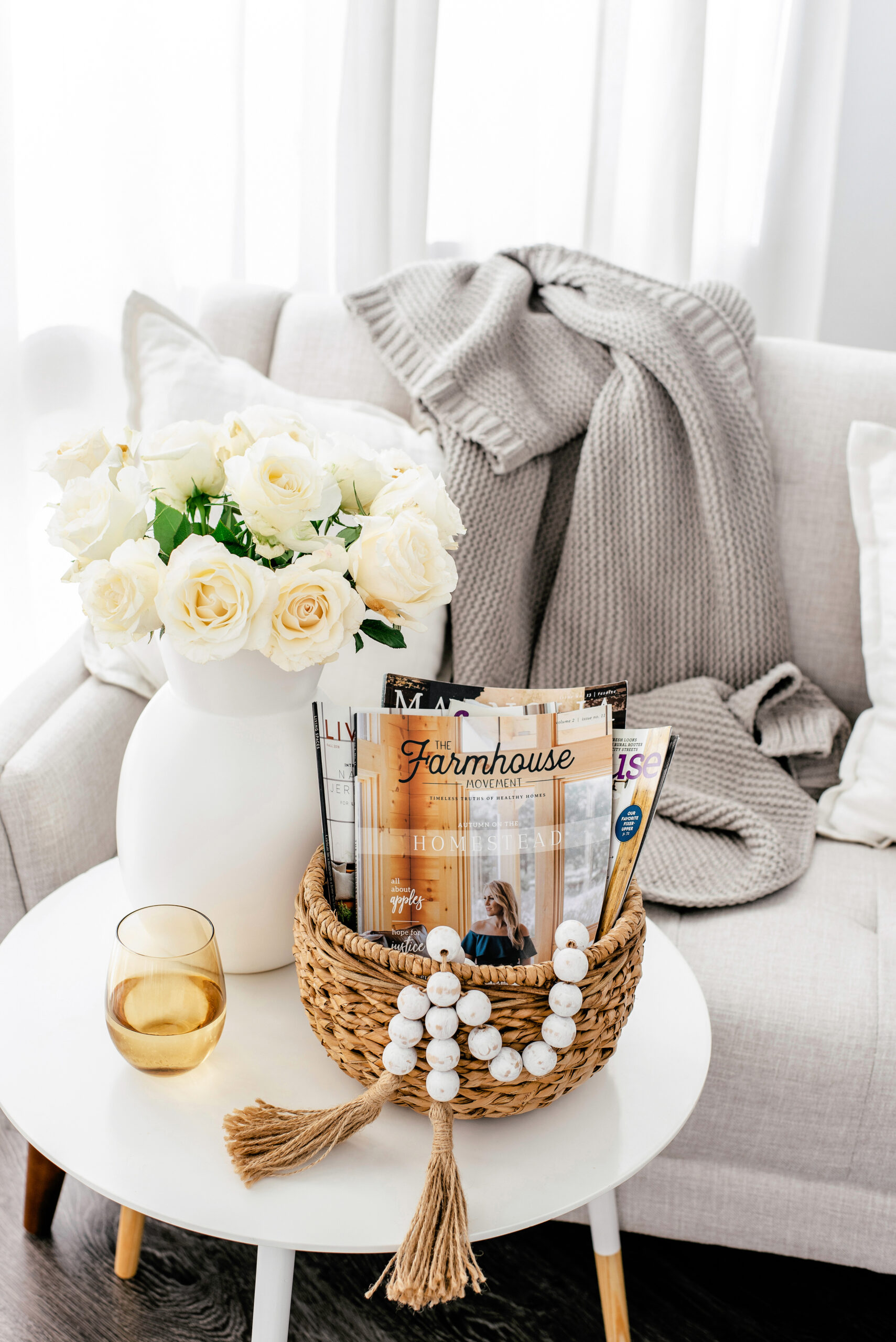 cozy living room with flowers, throw blanket on couch, and wicker basket on table with wine