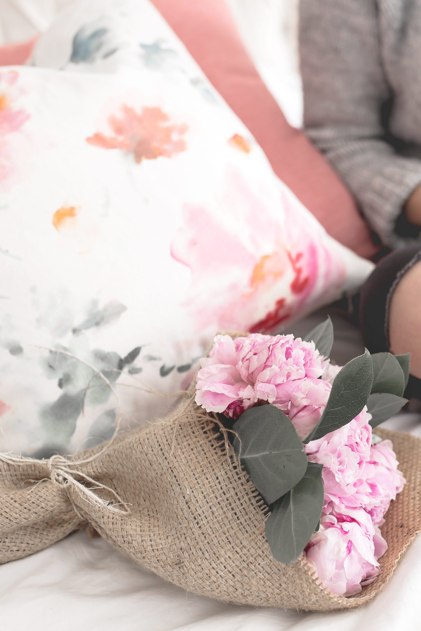 close up on oversized pillows, flowers, and a non descript woman sitting next to them