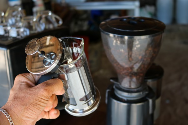 Woman holding French Press coffee maker in front of coffee bean grinder