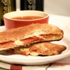 Pepperoni sticks on a white plate with a bowl of marinara sauce.