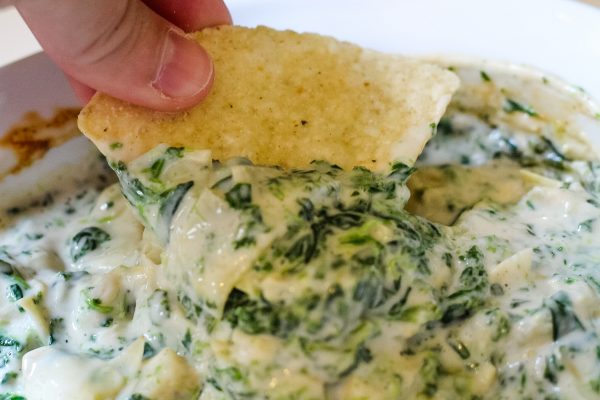 tortilla chip being dipped in artichoke and spinach dip