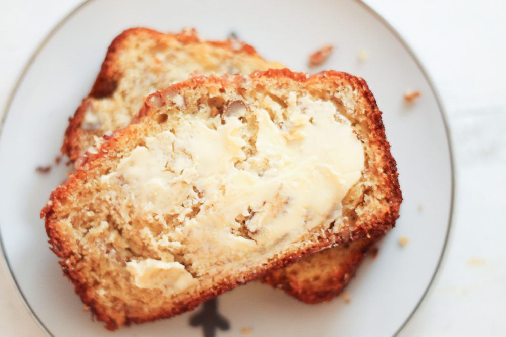 overhead view of two slices of buttered banana bread on a plate