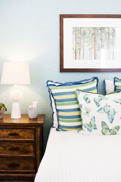 cozy bed with throw pillows next to a night stand with a lamp on it