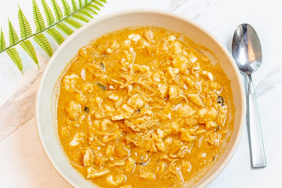 overhead view of a palm leaf, spoon, and bowl of chicken paprikash soup