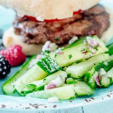 hamburger, mixed berries, and matchstick cucumber salad on a teal plate