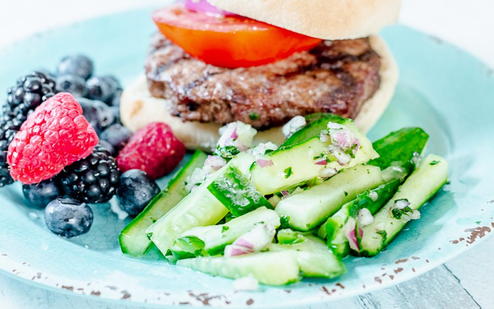 hamburger, mixed berries, and matchstick cucumber salad on a teal plate