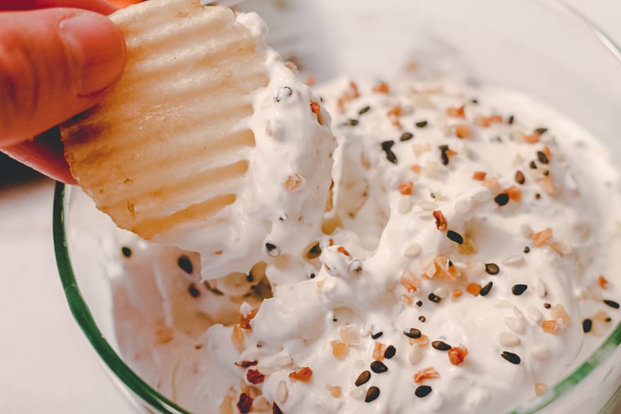 hand dipping a rippled chip into everything bagel dip