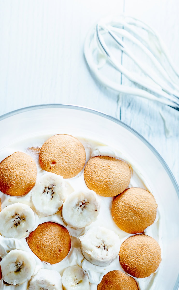 banana cream pudding in a trifle bowl next to a whisk