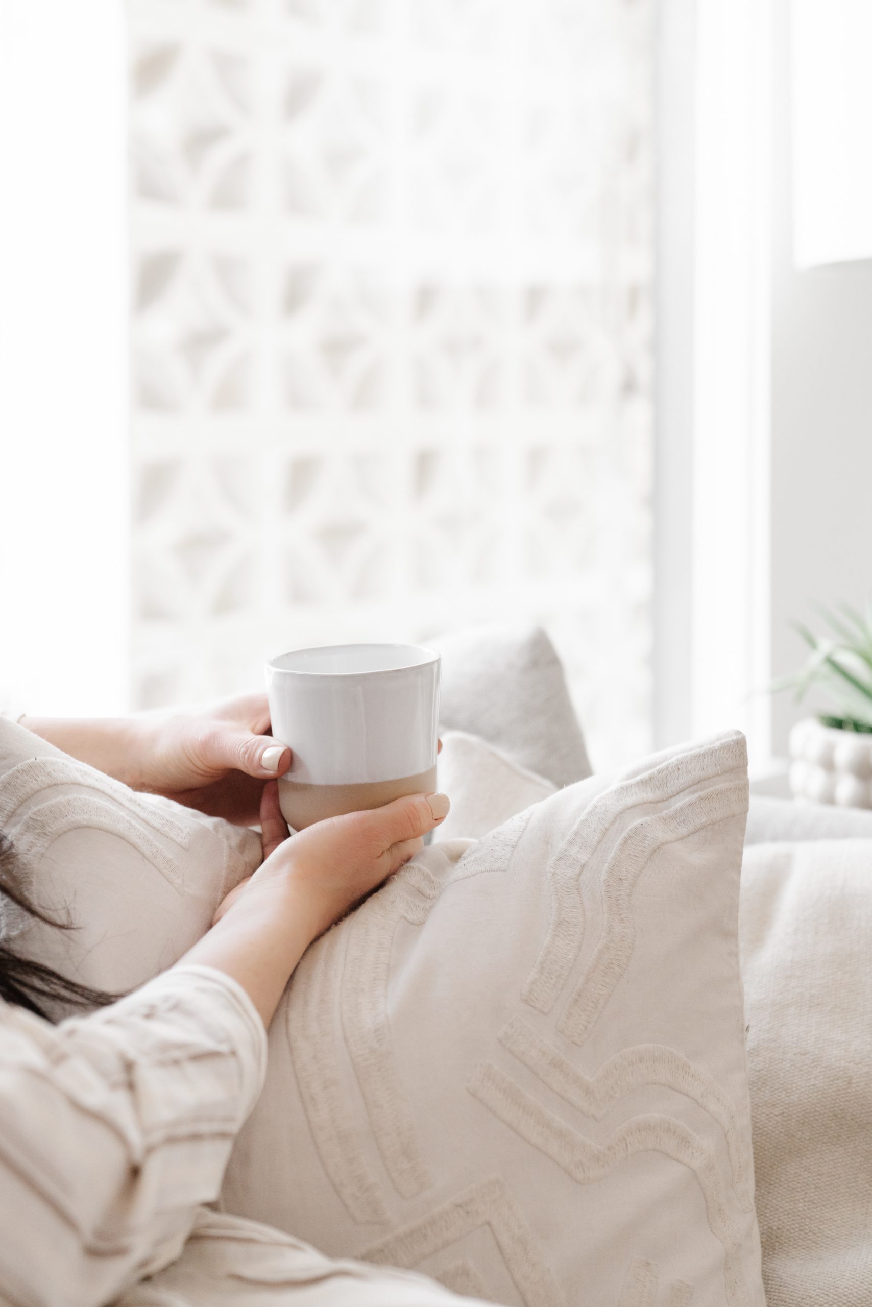 non-descript woman experiencing hygge on a cozy couch with a mug