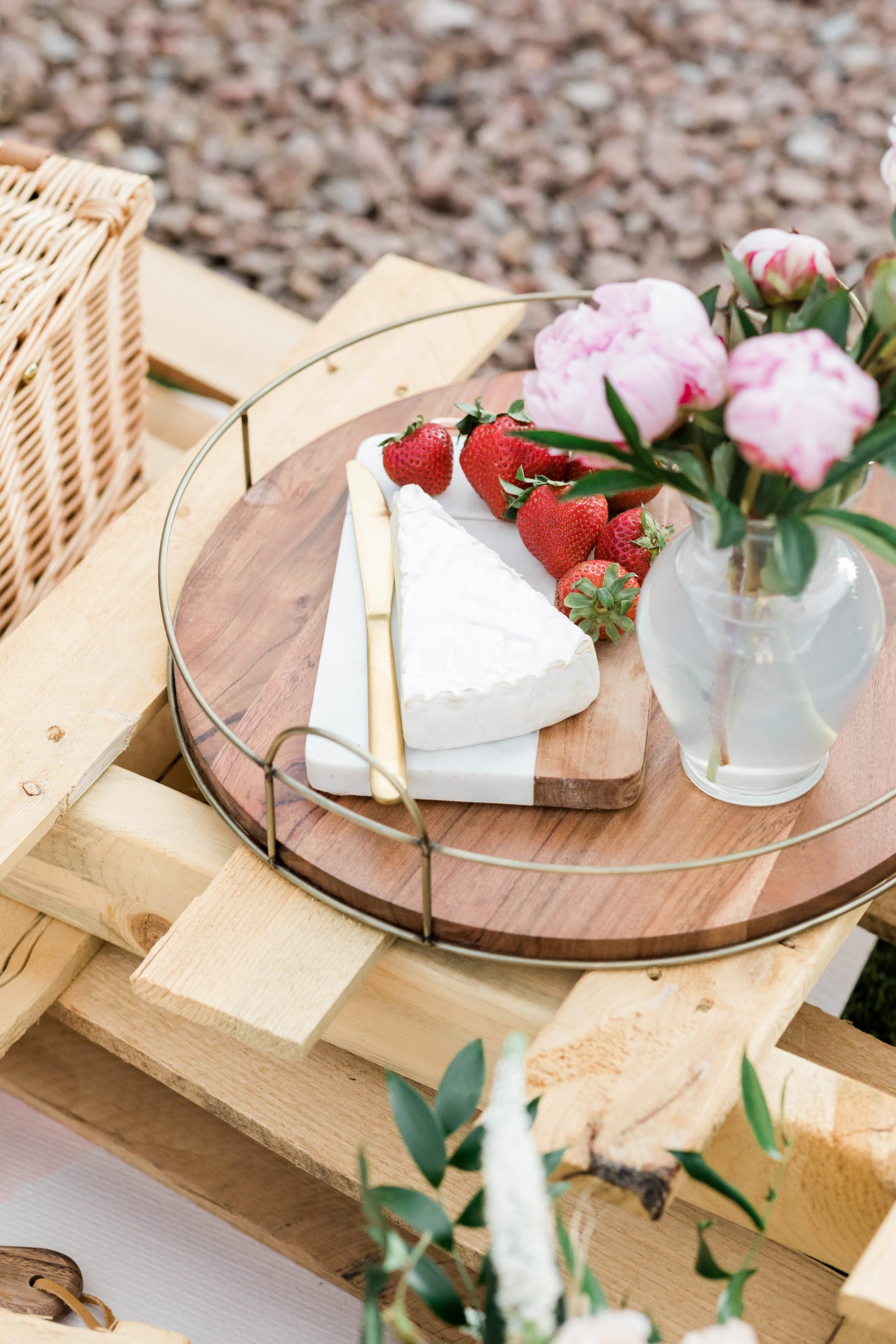 round wooden tray with cheese, strawberries, and flowers