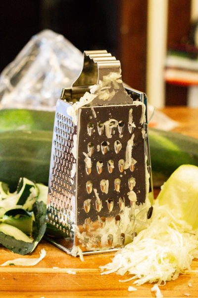 grater and shredded zucchini on a wooden cutting board