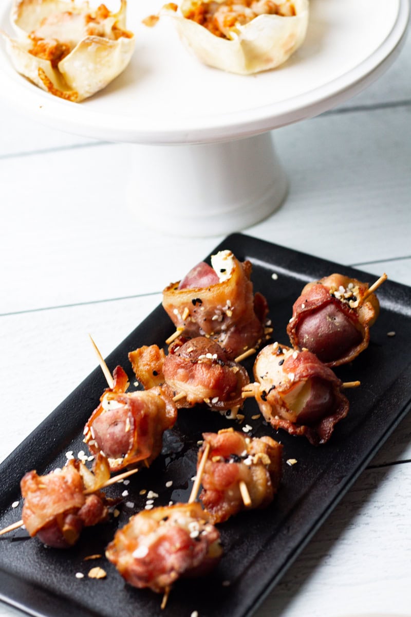 goat cheese, bacon, potato, and everything but the bagel seasoning appetizers on a black serving tray with a white cake stand in the background