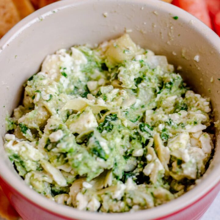 Red bowl with spinach, artichoke, and feta Mediterranean appetizer dip with pita chips and carrots