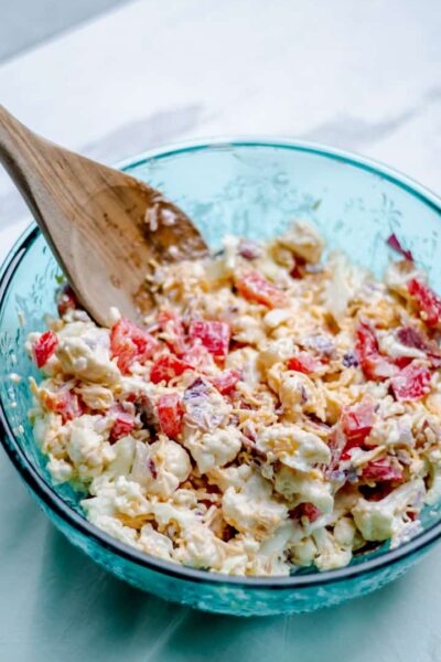large bowl of bacon cheddar cauliflower salad with a wooden spoon