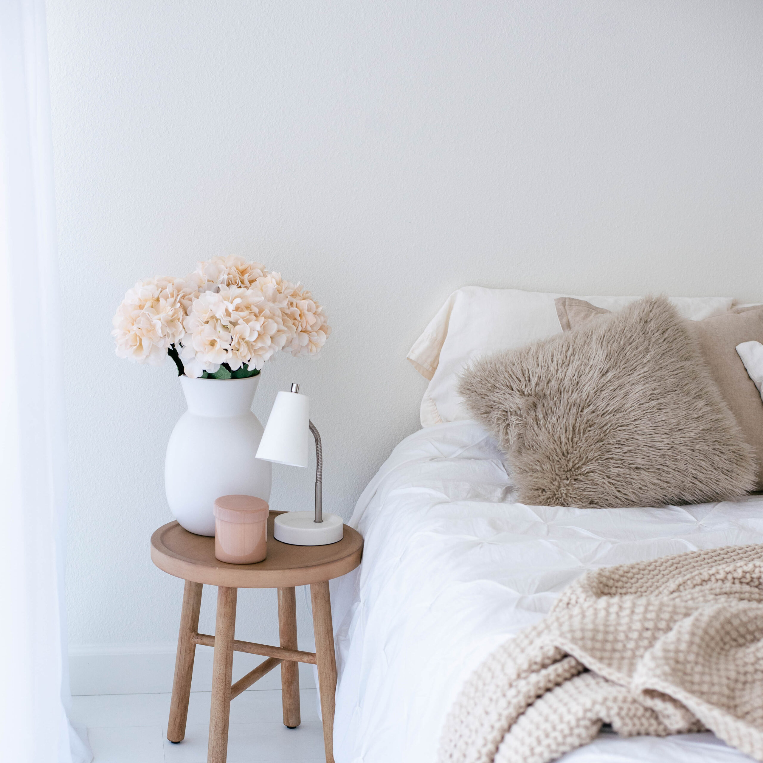 bed with throw pillows and a blanket next to a nightstand with flowers and a small lamp