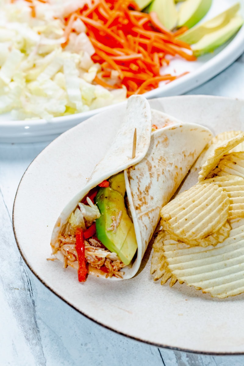 buffalo chicken wrap and potato chips on a white plate with a veggie tray