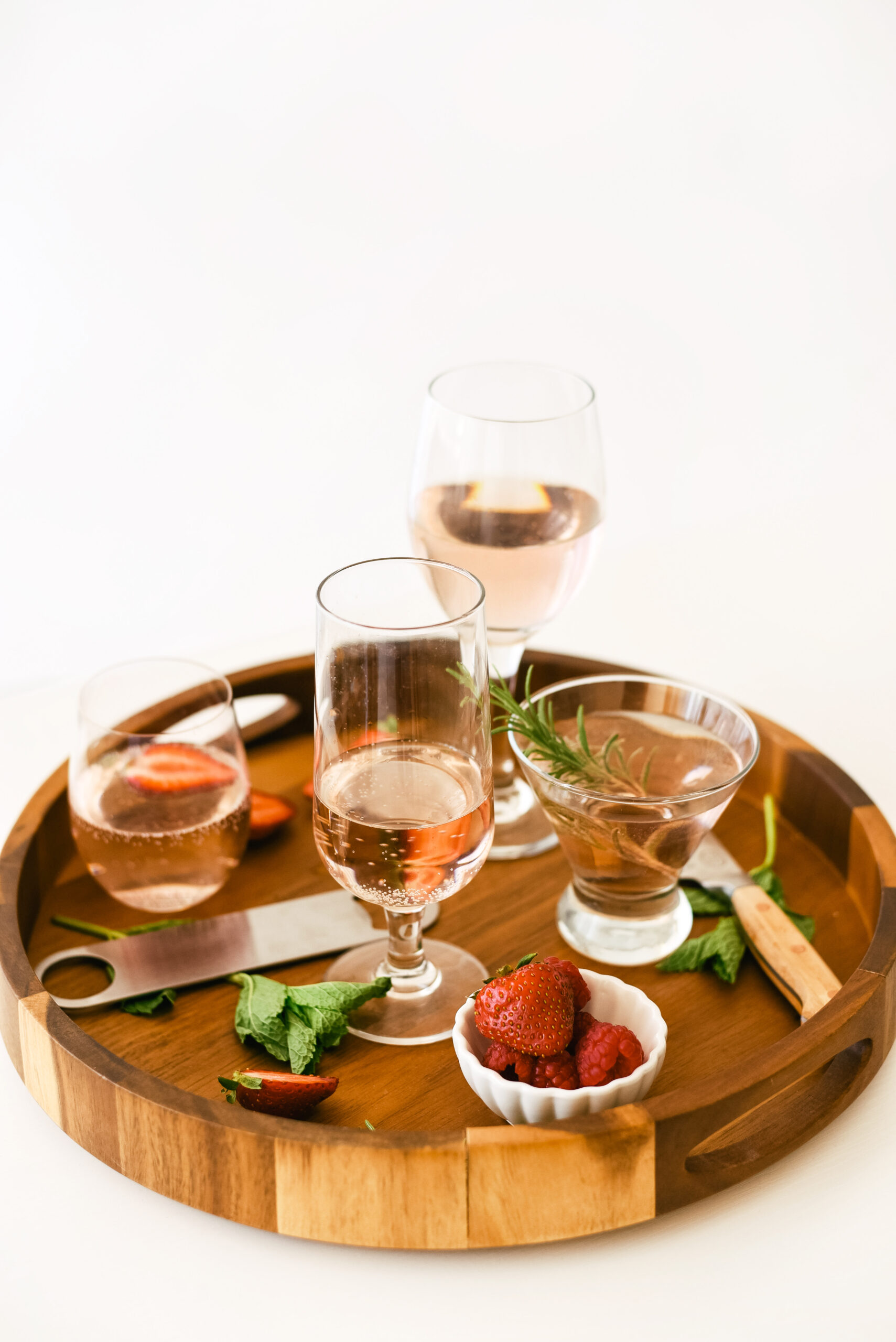 round tray filled with a variety of glasses of wine and a bowl of strawberries