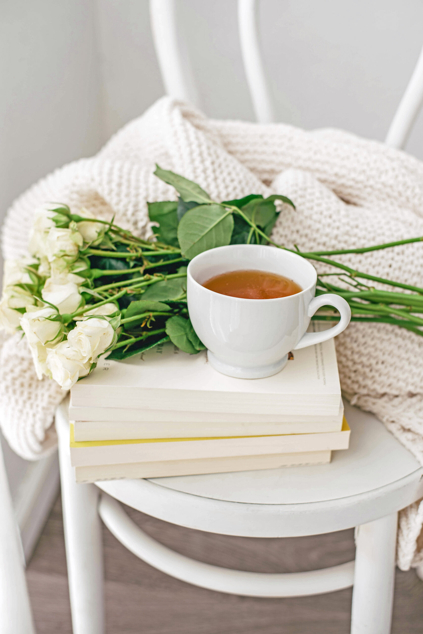 cup on tea and roses setting on top a pile of books on a chair