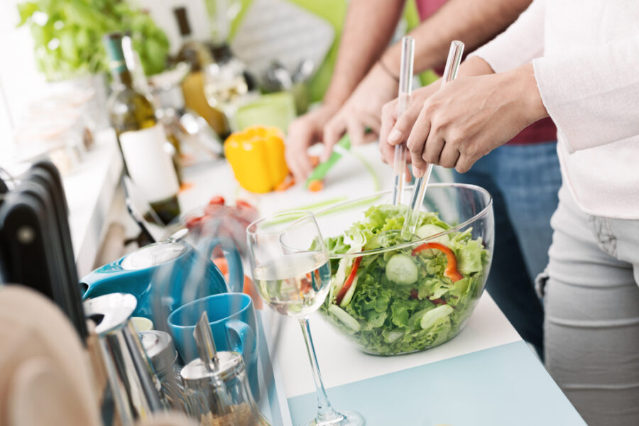 Couple cooking together in the kitchen, the woman is mixing salad and the man is chopping vegetables in the background, daily life and relationships concept