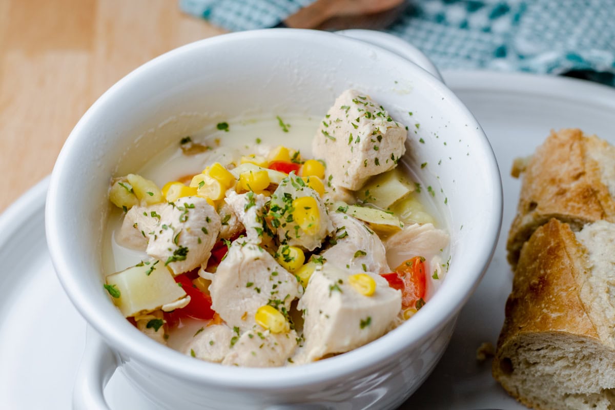 white bowl with Boma Chicken Corn Chowder and a slice of crusty bread