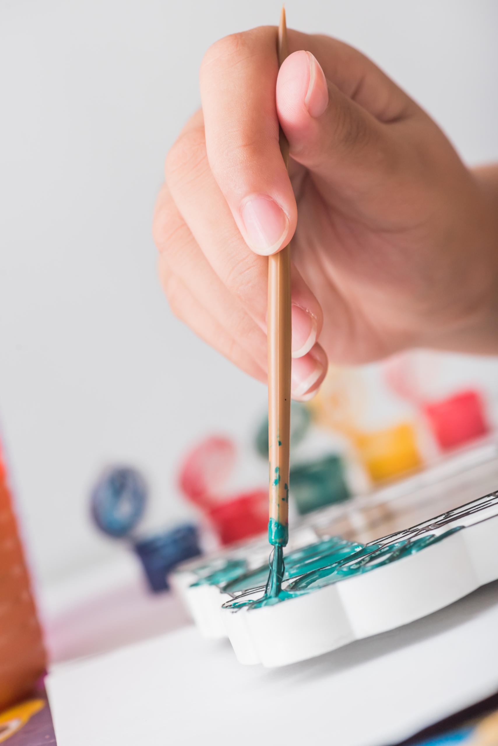 non descript hand dipping an artist paint brush into a pallet of paints