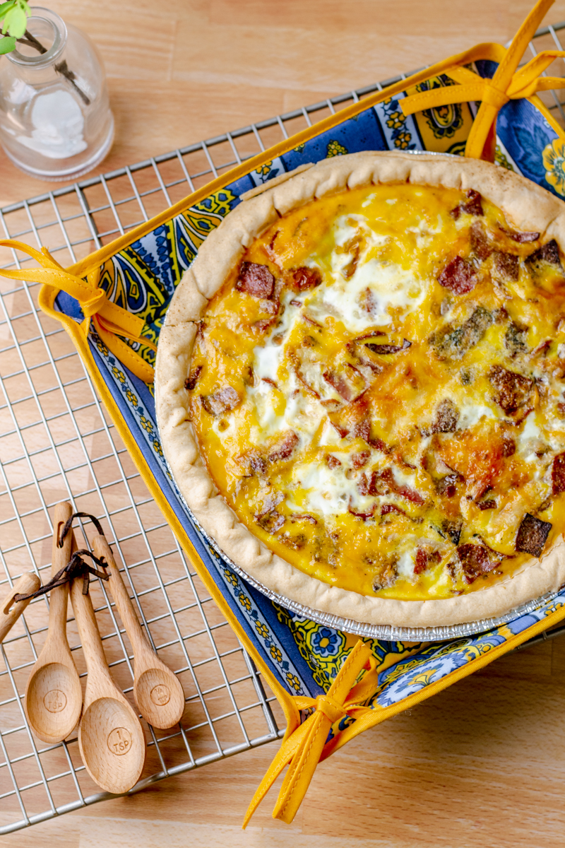 overhead view of bacon quiche on a cooling rack with wooden measuring spoons next to it