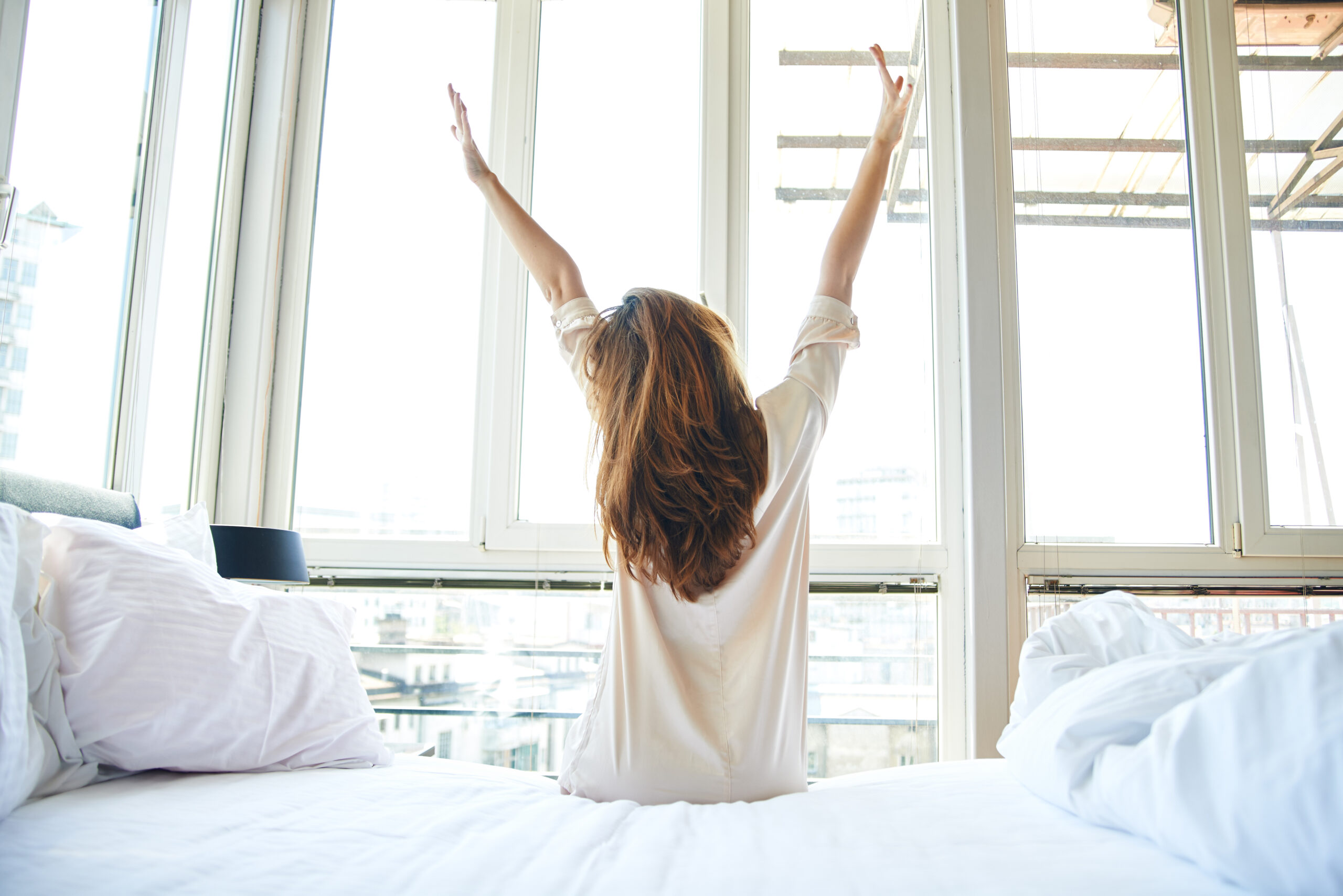 woman stretching as she wakes up and faces a large window