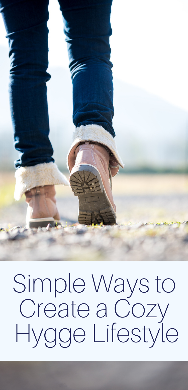 Feet of a woman in jeans and boots walking along a rural path away from the camera with text overlay "simple ways to create a cozy hygge lifestyle"