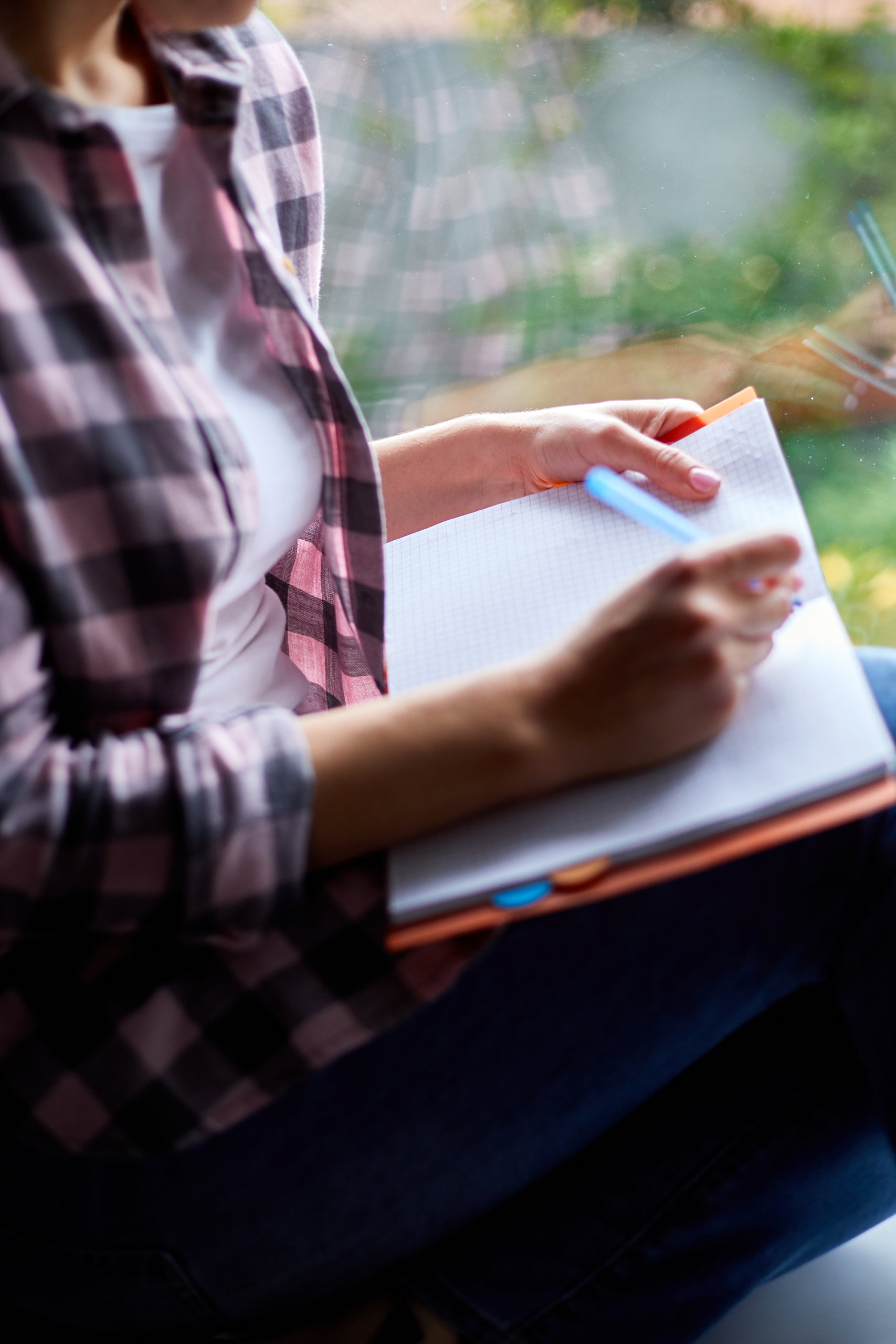 Woman, sitting at window at home, writes in notebook goals