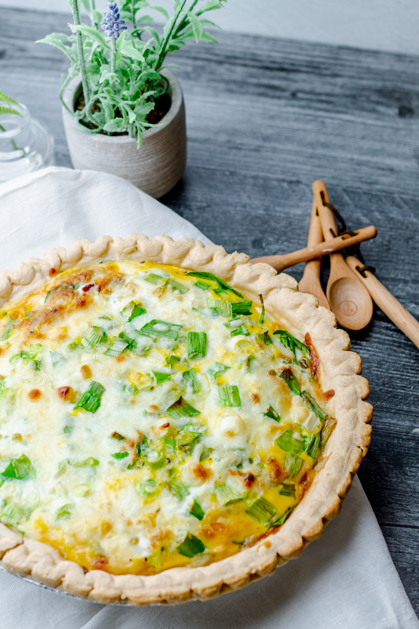 bacon and spinach quiche on a white cloth with a lavender plant and set of wooden measuring spoons