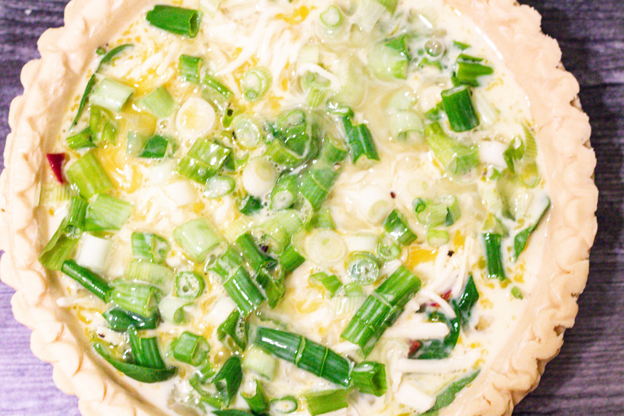 unbaked pie crust with egg and veggies and cheese