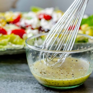 close up of a DIY Mediterranean salad dressing being hand whisked with a Greek Salad in the background