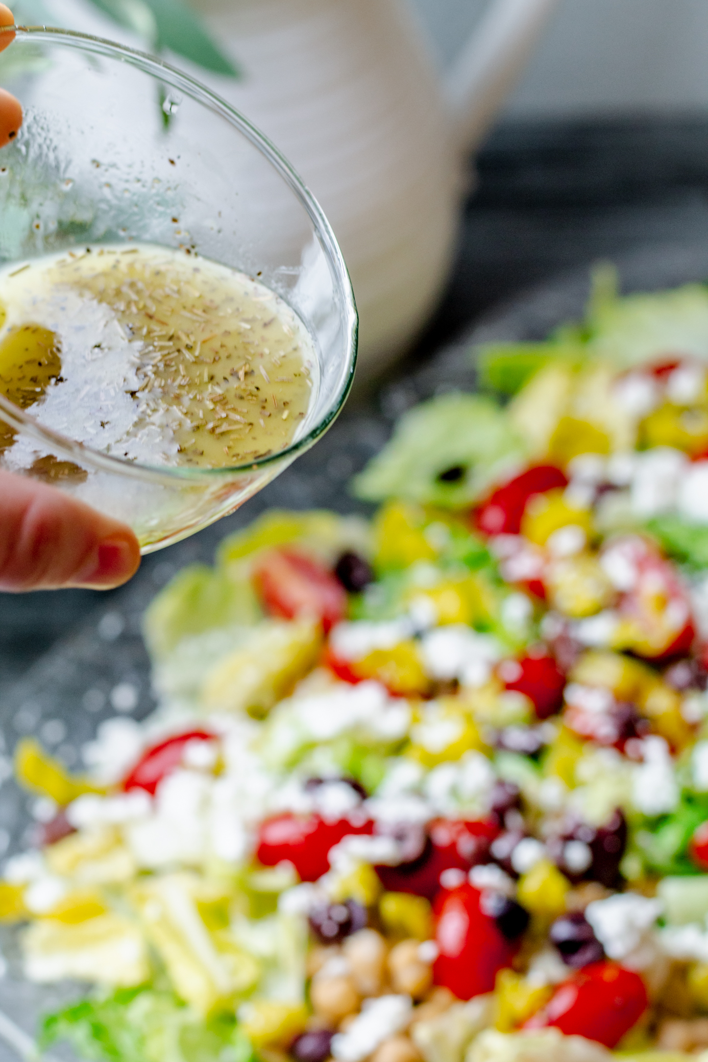 non descript hand pouring homemade Mediterranean Salad dressing over a Greek salad