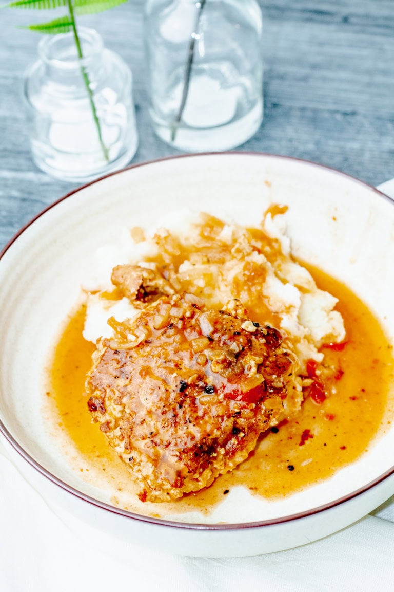 overview of a bowl filled with turkey salisbury steak, mashed potatoes, and gravy next to two glass vases