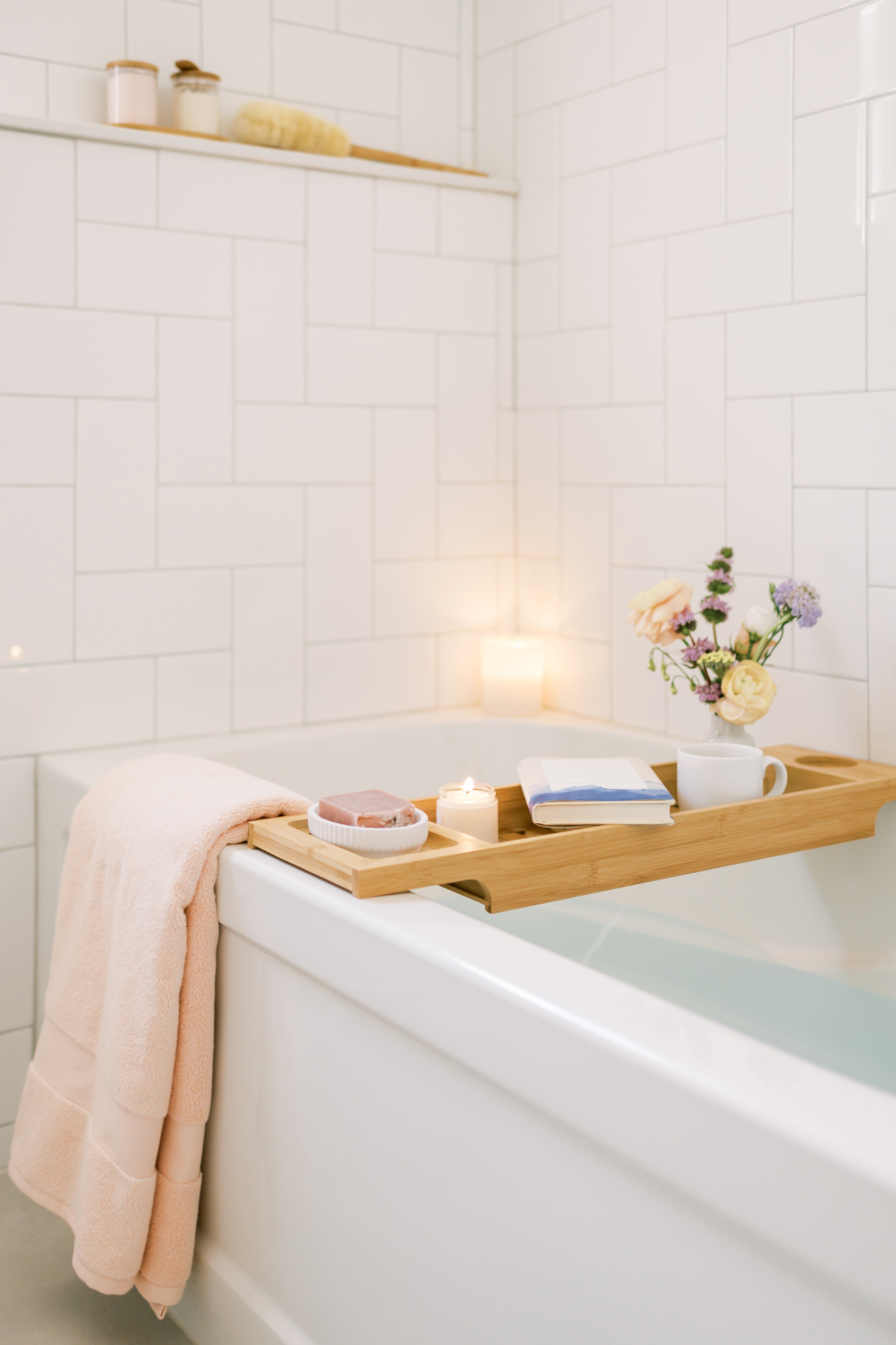 Bath tray filled with a book, candle, flowers, and soap over a filled tub