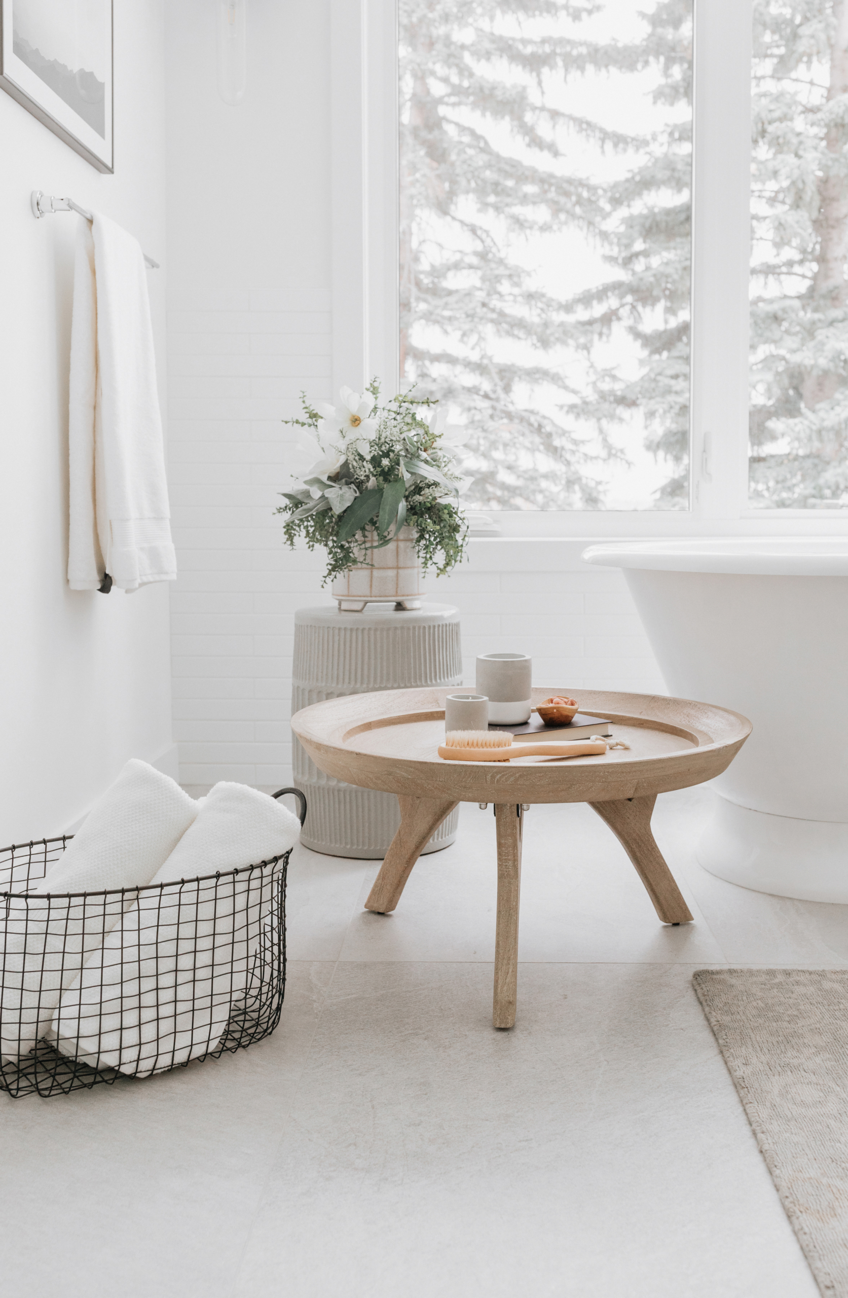 Relaxing bathroom scene with tub, spa tray, wire basket of towels, and plant on a garden stool