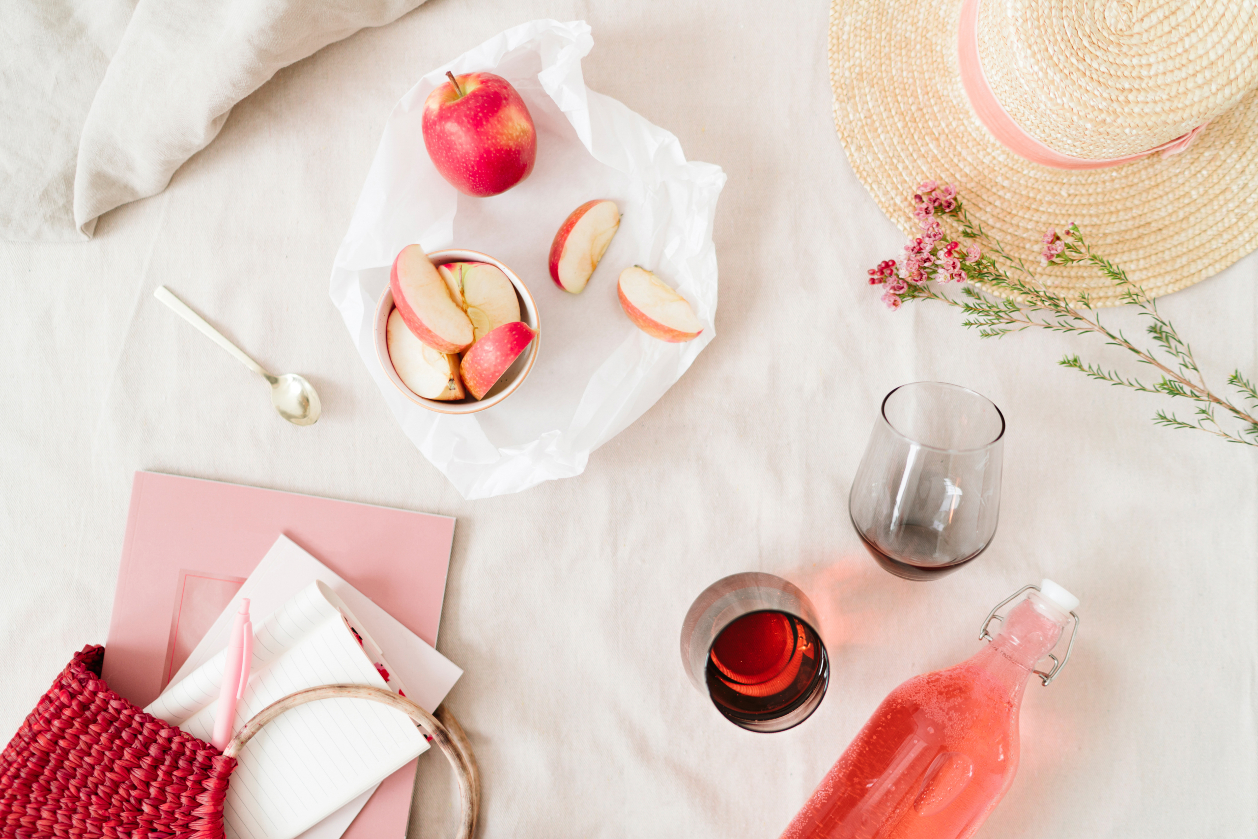 picnic of fresh apples and wine glasses with a straw hat and flowers in the scene