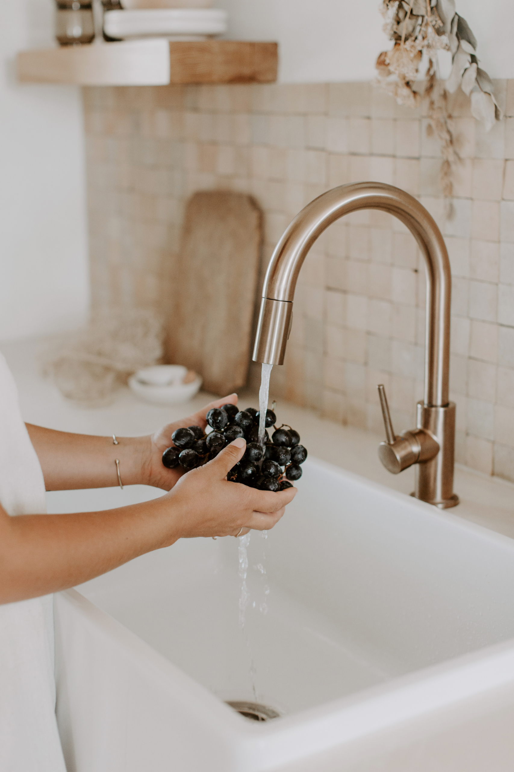 non descript woman washing a bunch of grapes at a kitchen sink