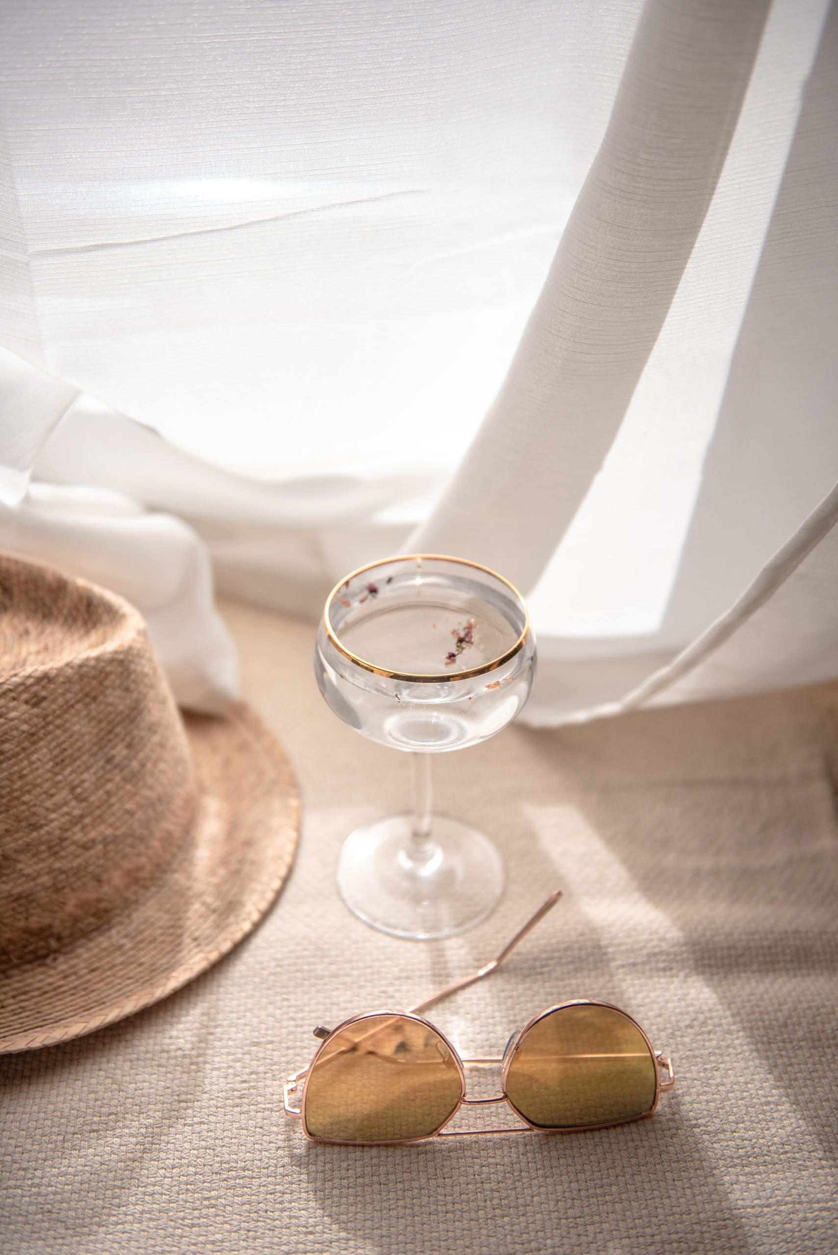 vacation scene with straw hat, champagne glass, and sunglasses on a beach blanket