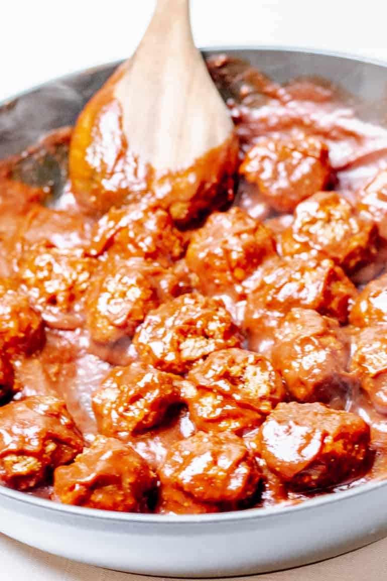 close up of a skillet filled with bbq meatballs being stirred by a wooden spoone=