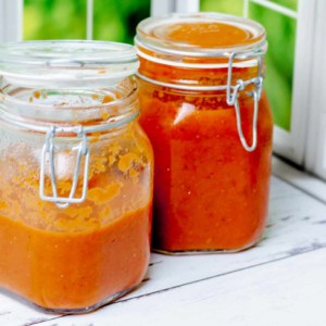 two glass jars of homemade tomato sauce in front of a window
