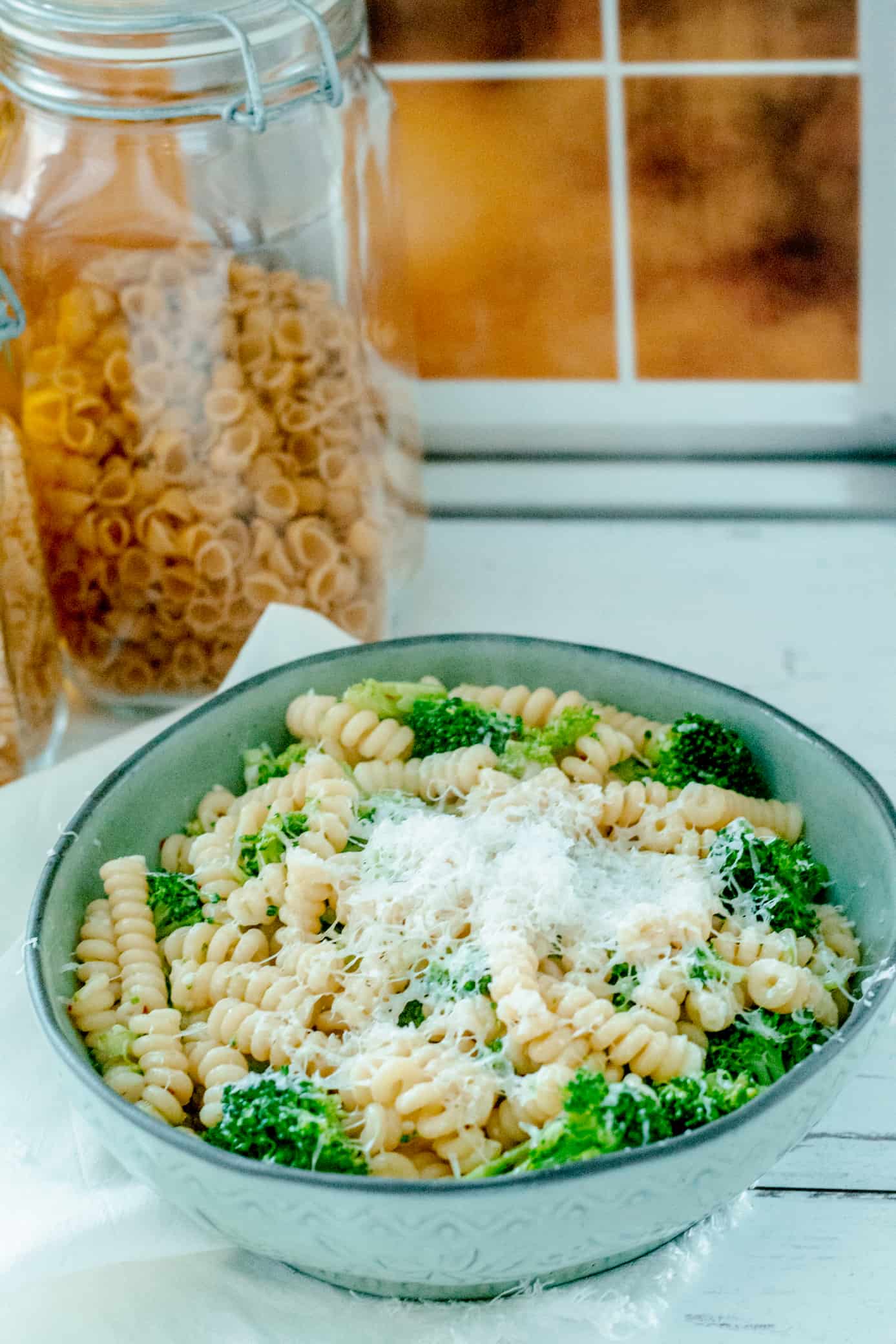 a bowl of Italian broccoli pasta in front of a window with two glass canisters of pasta