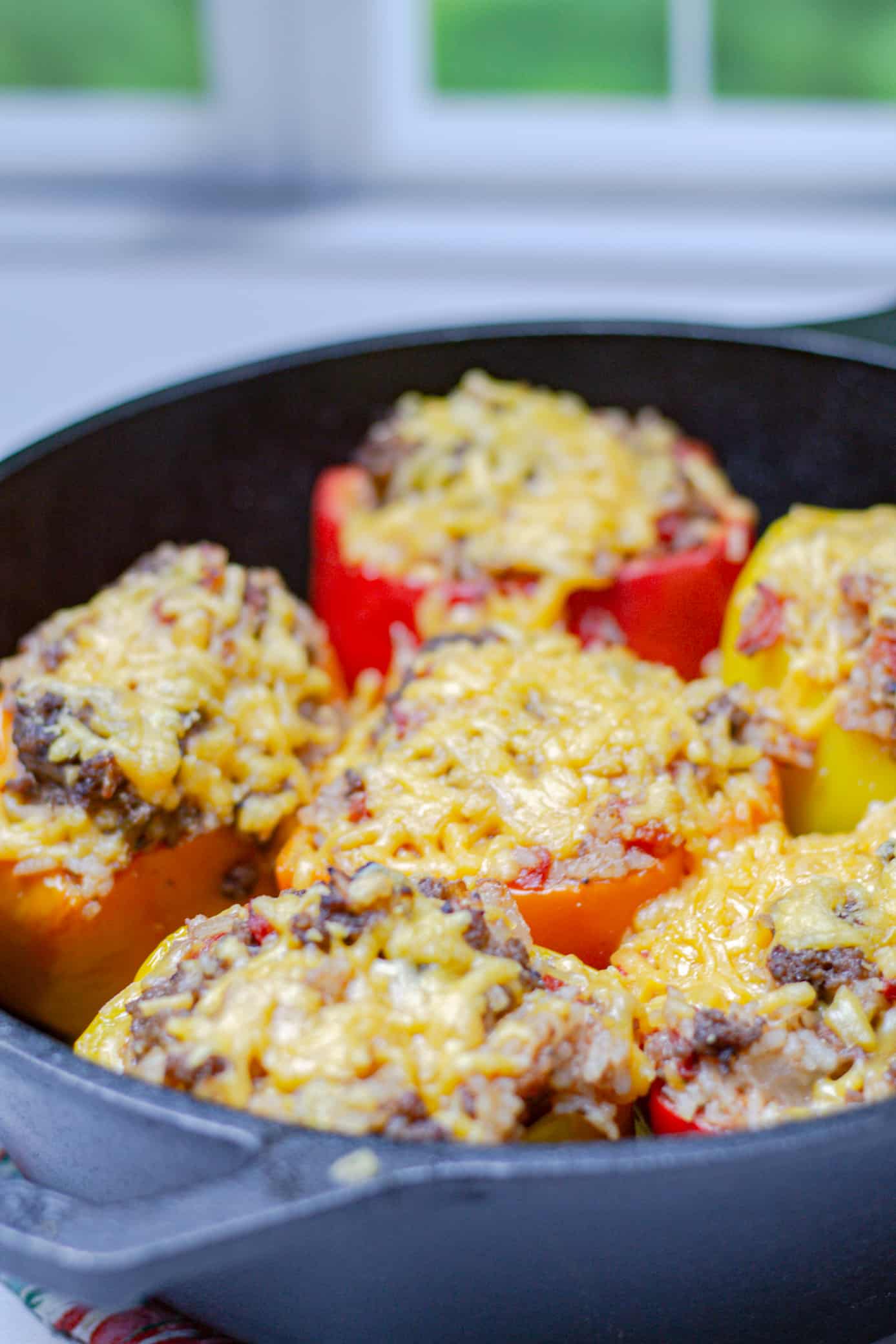 pan of 5 crisp beef stuffed peppers smothered in cheese with a window in the background